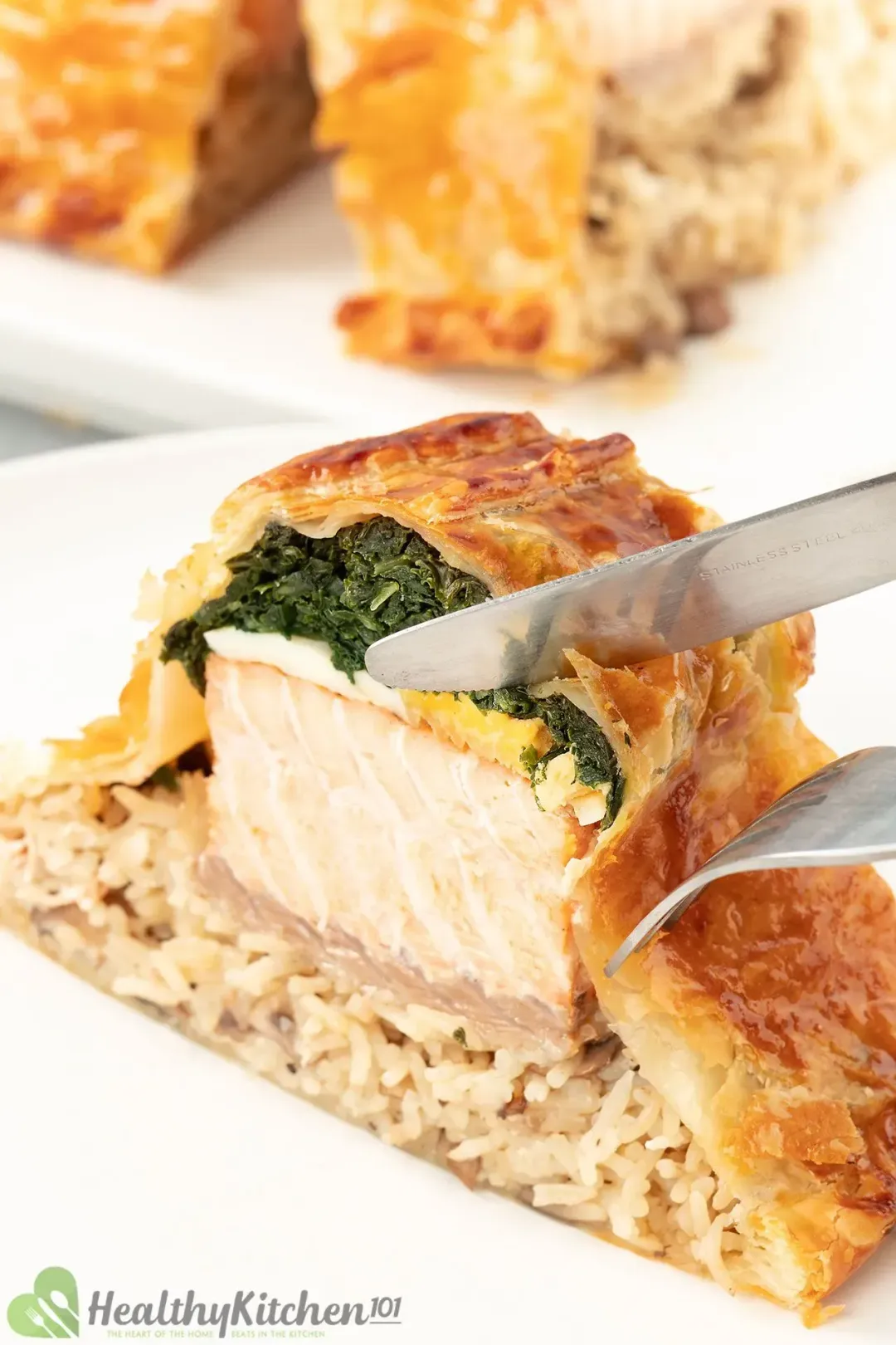 A slice of salmon coulibiac with layers of cooked kale, eggs, salmon, and rice about to be sliced