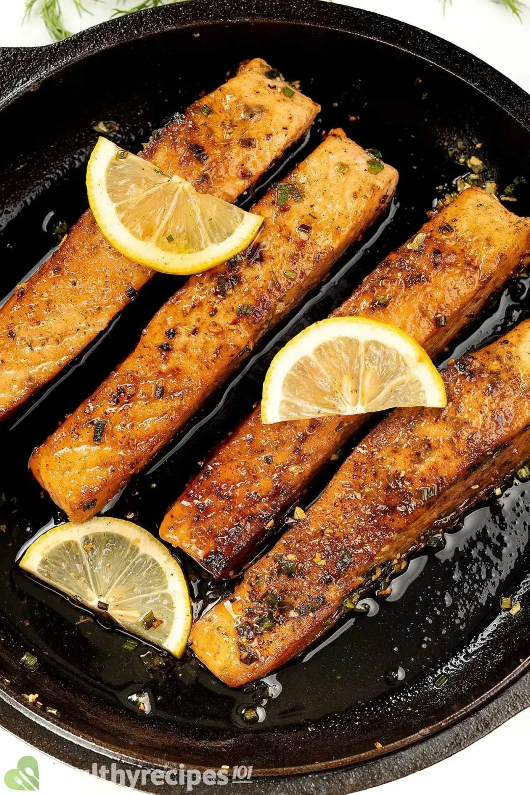 In a glossy cast iron skillet of butter sitting four slices of charred salmon Meuniere filet garnished with lemon slices