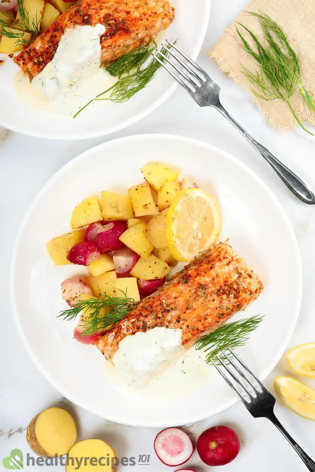 Two plates of salmon, potato cubes, radish cubes, and dill decorated by halved potatoes, halved radishes, two forks, and a tablecloth
