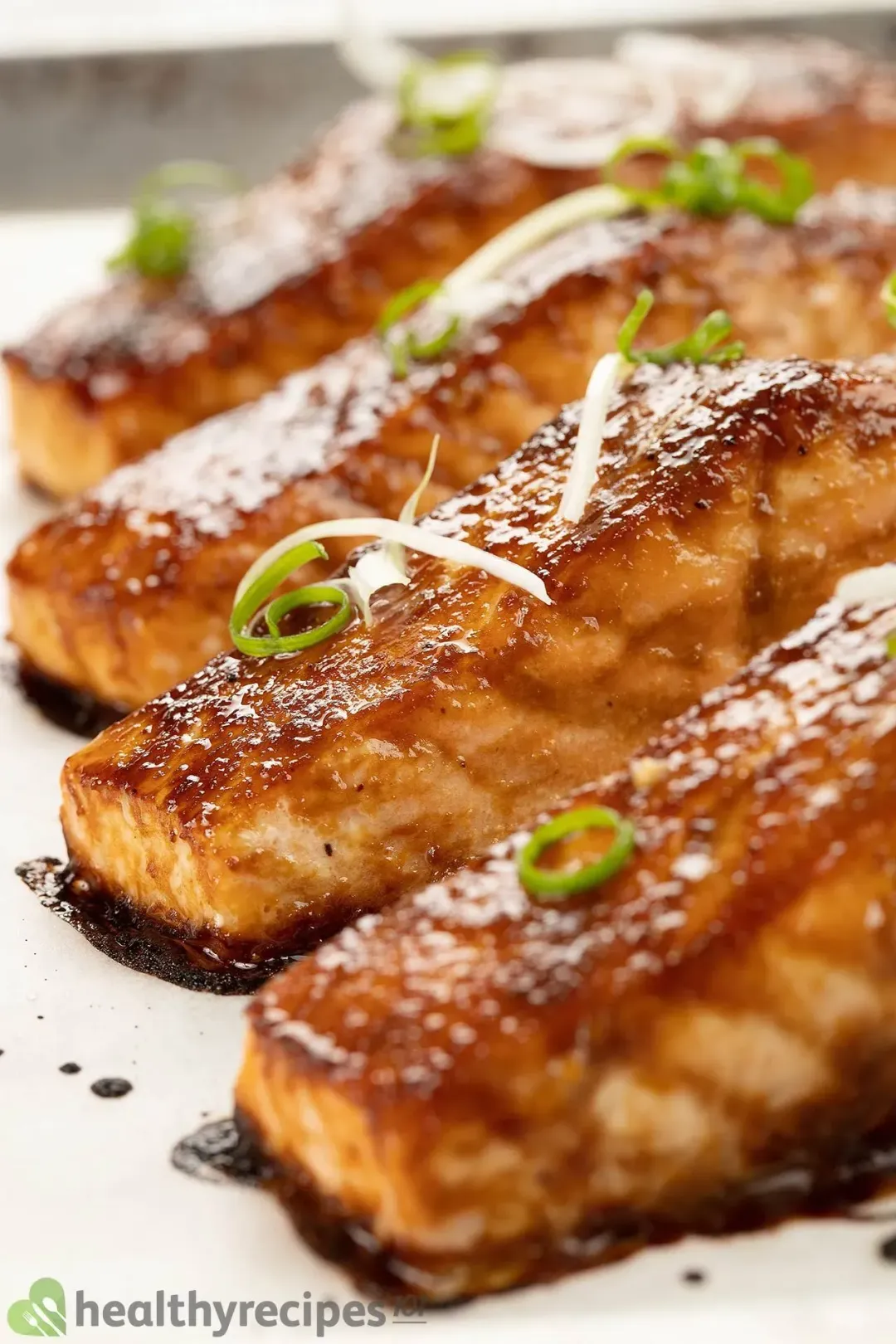 A close-up shot of salmon fillets covered in a glossy brown miso sauce and garnished by a few chopped scallions
