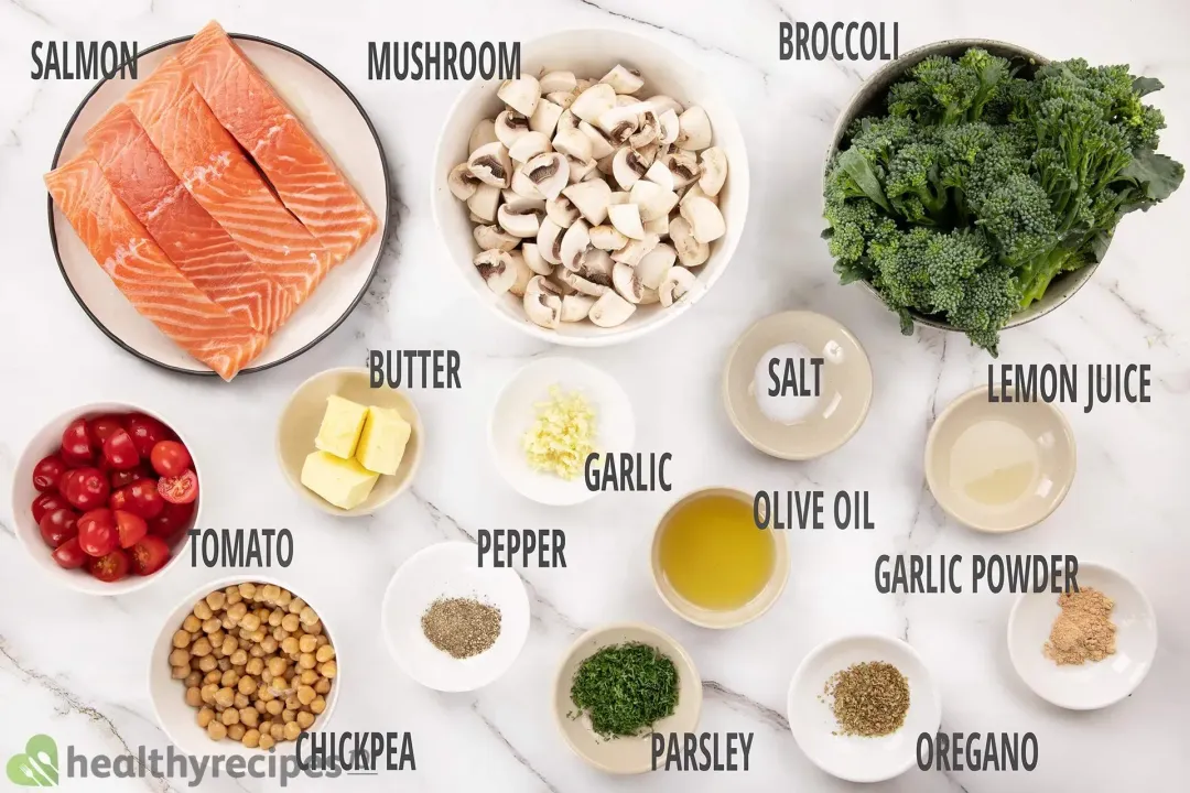 A plate containing four raw salmon fillets, a bowl of sliced white mushrooms, a bowl of broccolini, a bowl of chickpeas, and a bowl of halved cherry tomatoes laid near various condiments