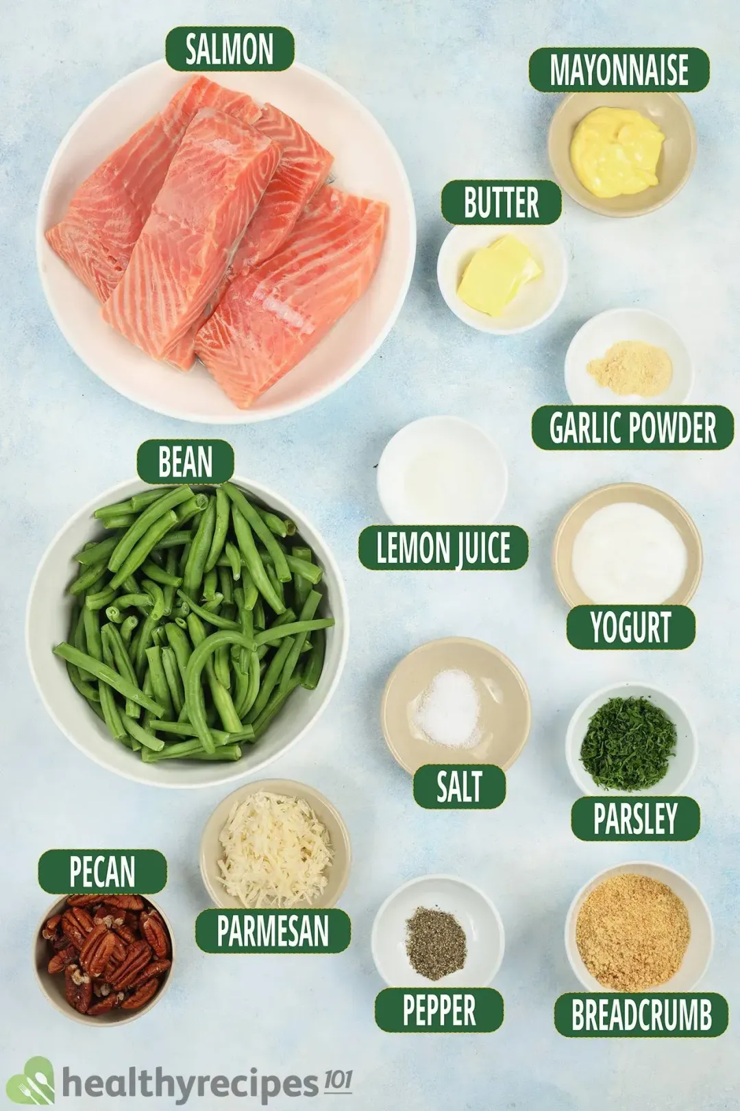 A full display of ingredients placed in separate bowls, including salmon, mayonnaise, butter, garlic powder, bean, lemon juice, yogurt, salt, parsley, pecan, parmesan, pepper, and breadcrumb.