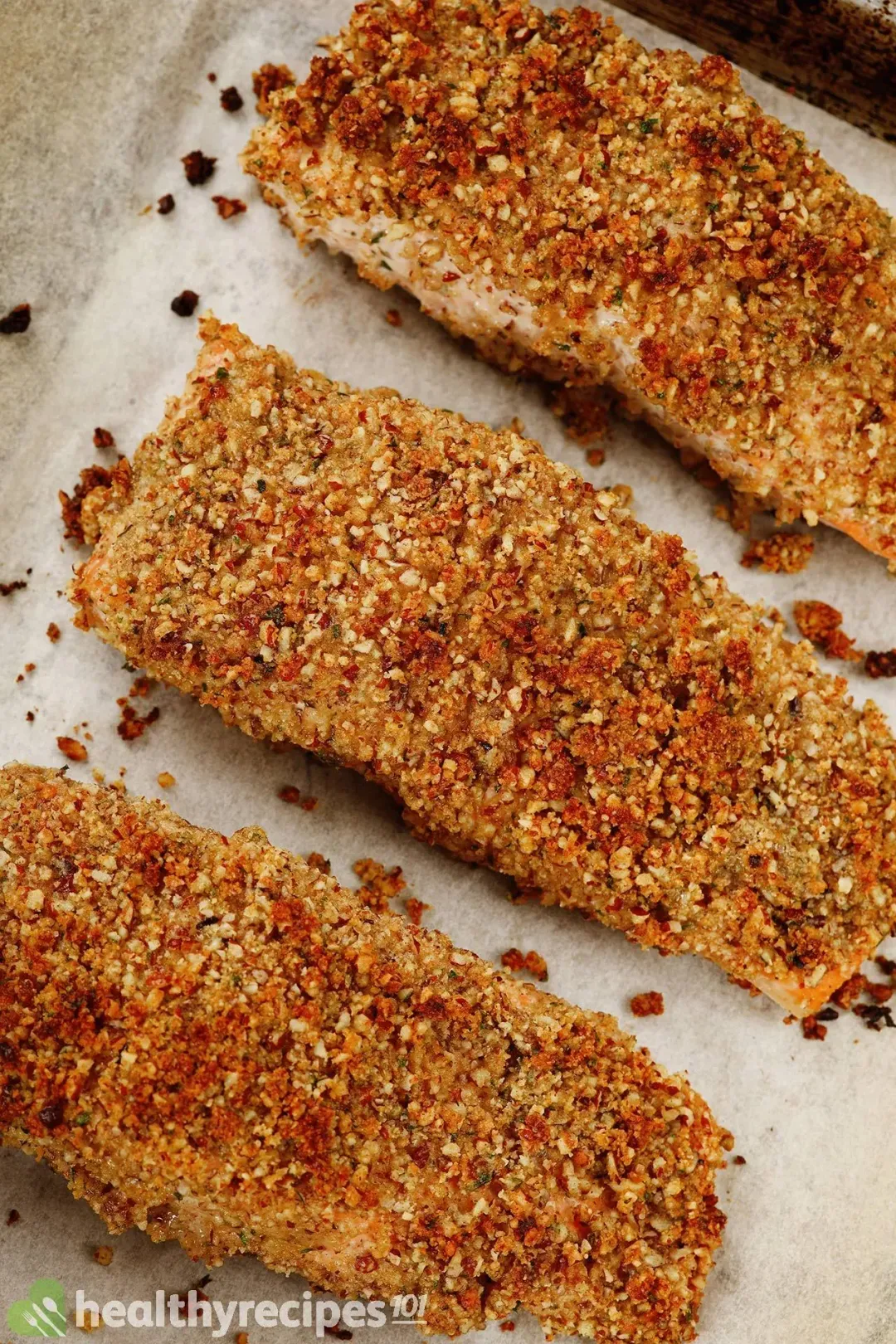 Three salmon filets that are fully dredged in pecan crust and placed on a parchment paper.