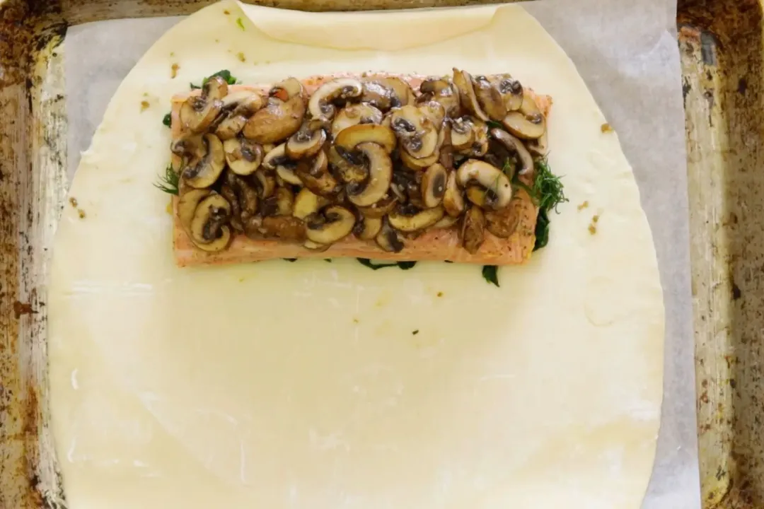 Layers of spinach, salmon, and cooked mushrooms laid on top of a puff pastry dough