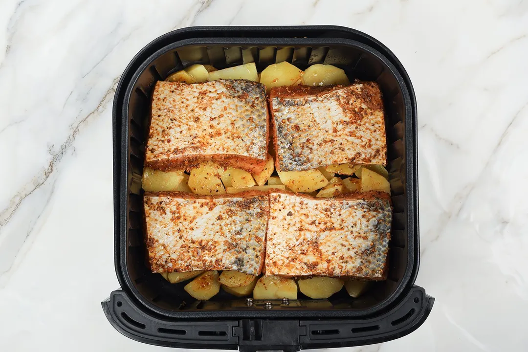 four salmon fillets bed on potato cubed in an air fryer