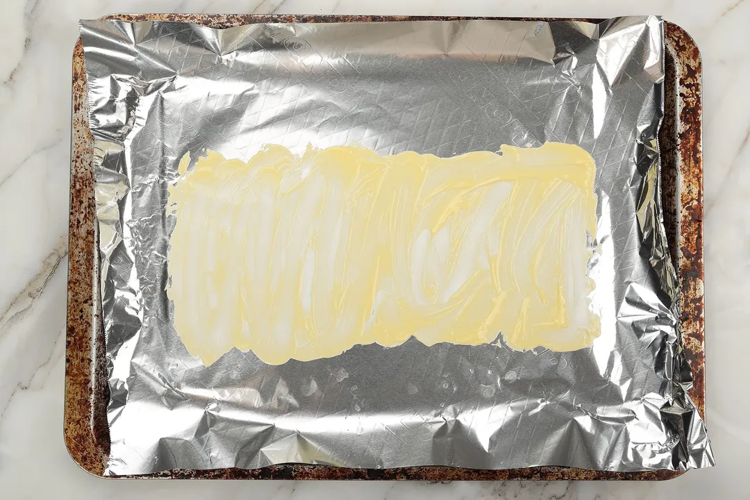 A baking tray lined with foil with melted butter spreaded all over the foil