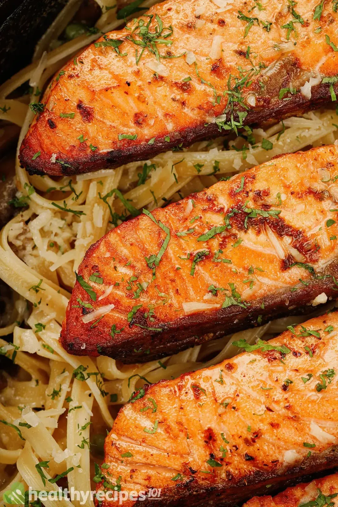 Three cooked salmon fillets with some sprinkles of chopped parsley on top laid on fettuccine pasta