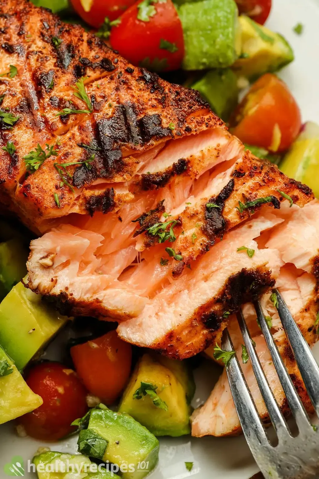 A close-up shot of a piece of seared salmon on top of avocado and tomato salsa