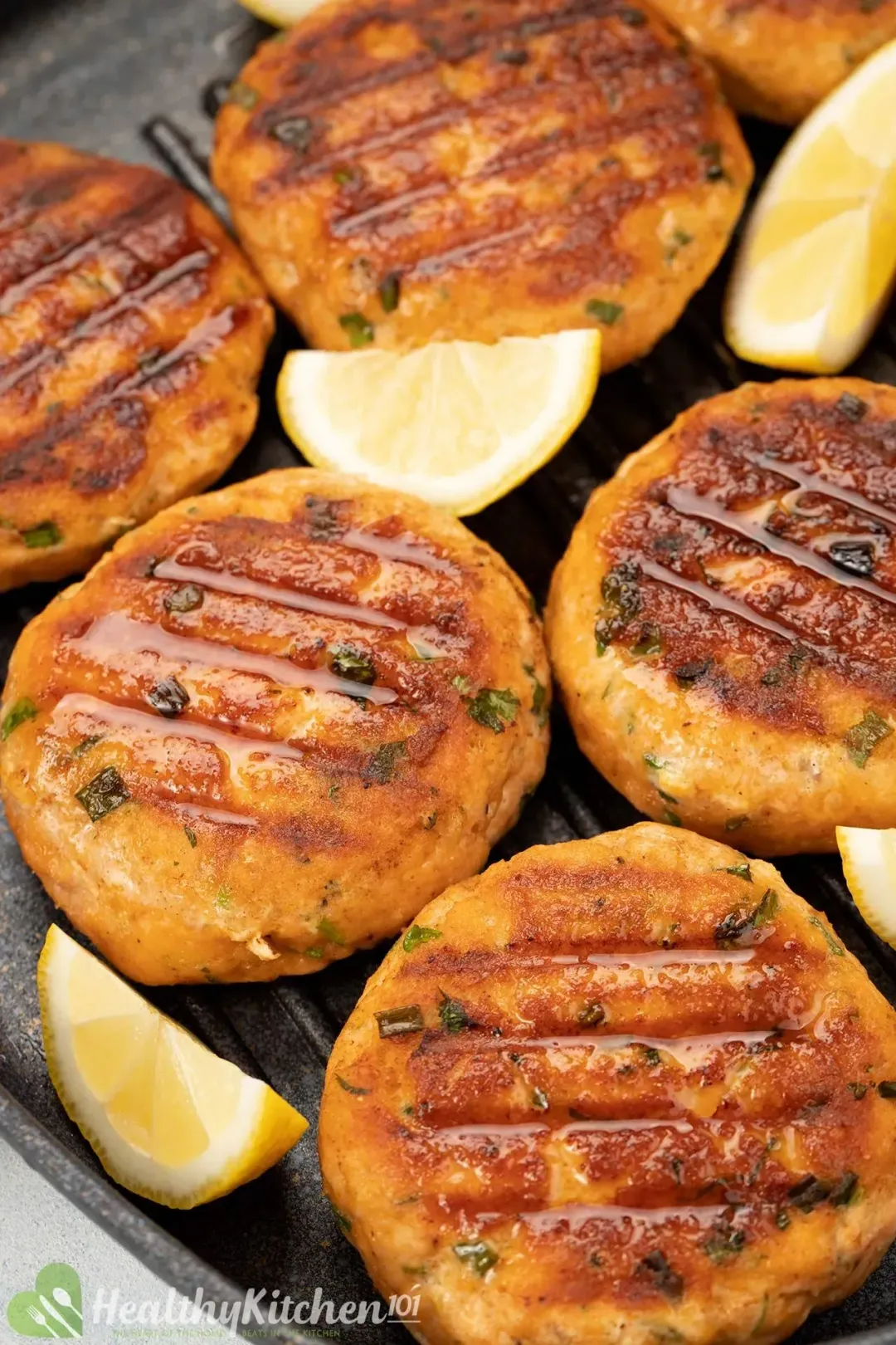 Some salmon croquettes with lemon slices in a black skillet.