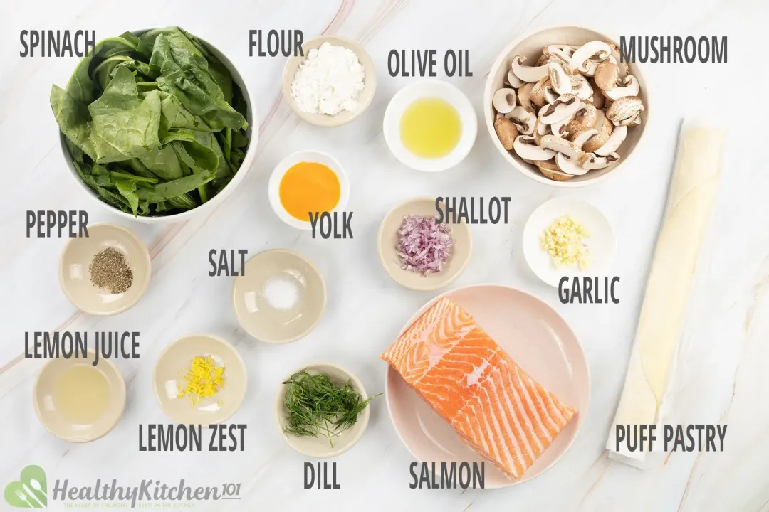 A plate of salmon fillets, a bowl of sliced crimini mushroom, a bowl of spinach, and some puff pastry laid near various spices