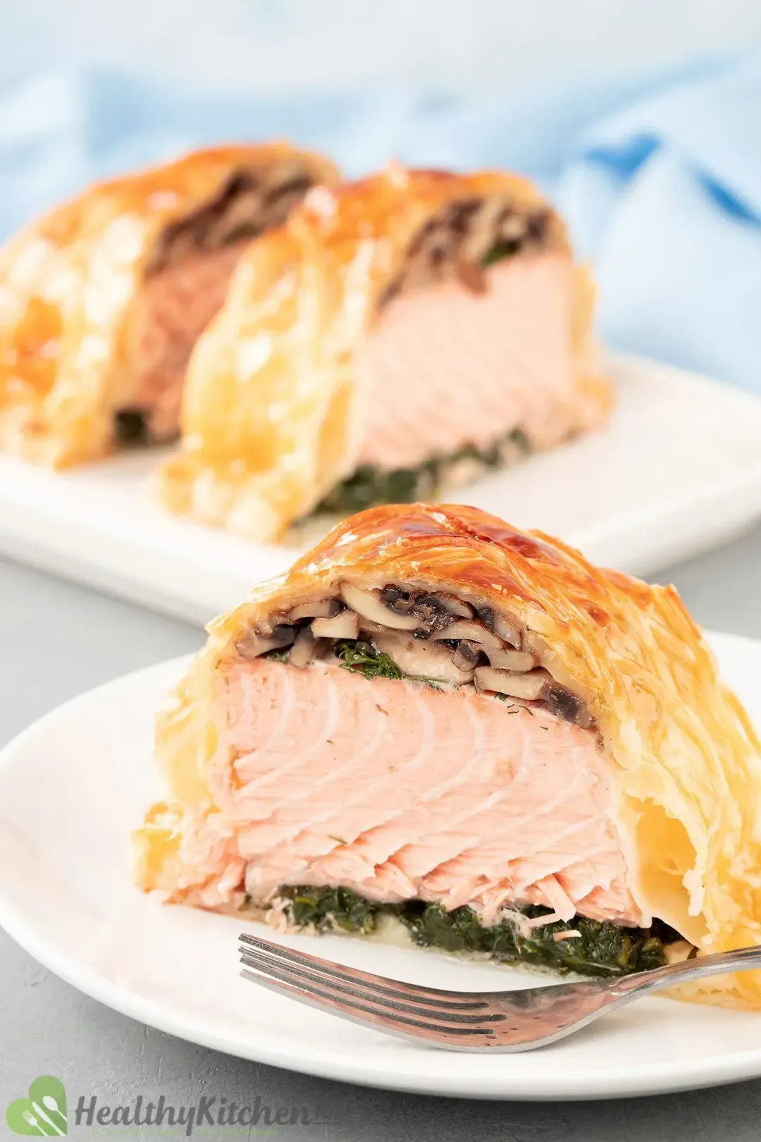 A white plate containing a piece of  salmon en croute placed next to a fork