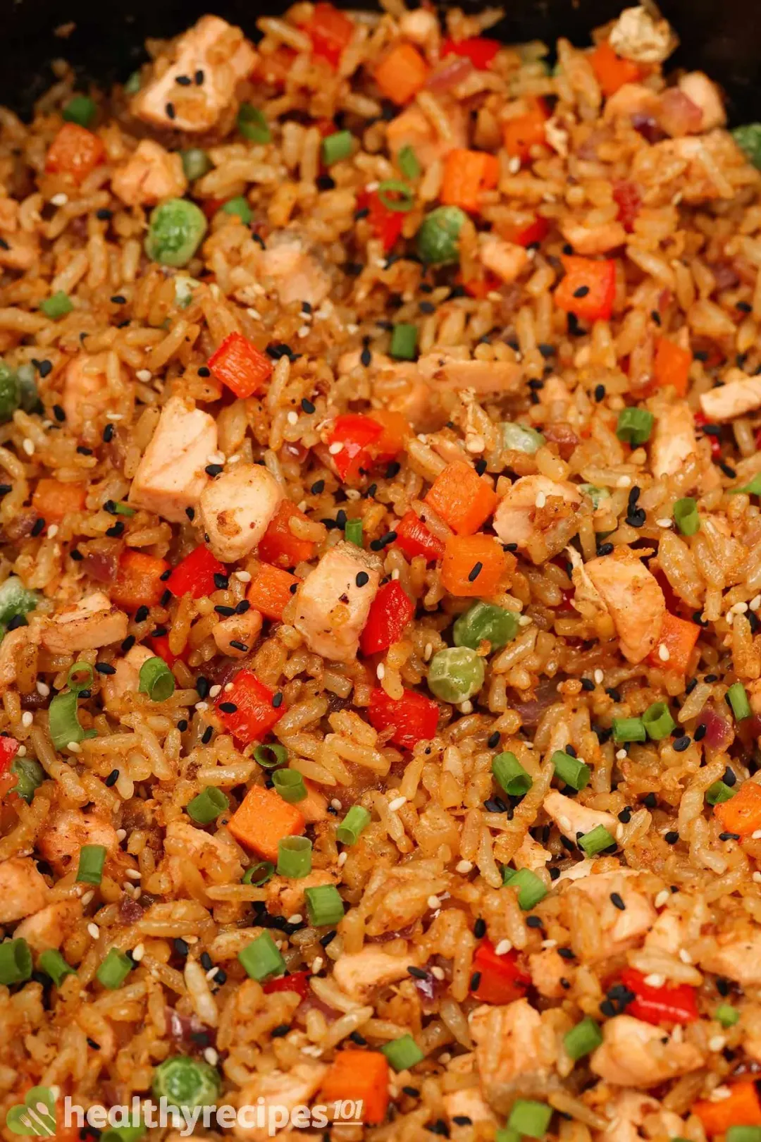 A skillet of golden brown fried rice speckled with peas, carrots, peppers, and salmon cubes