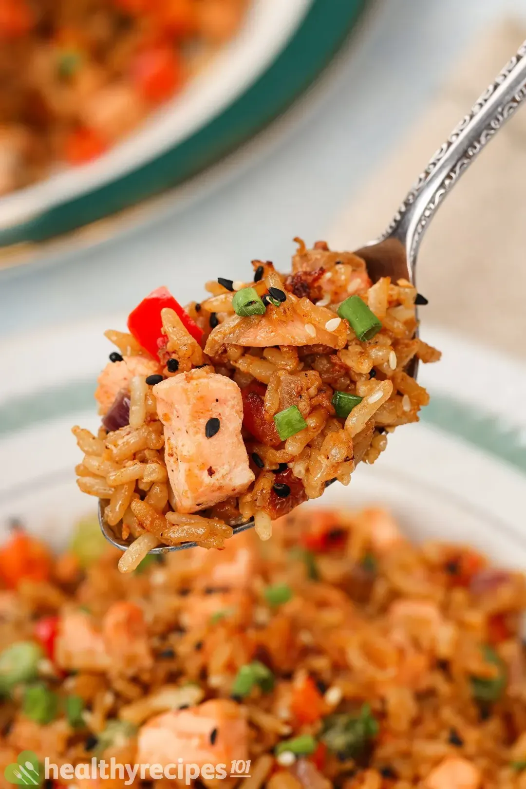 A spoonful of golden brown fried rice with salmon, rice, green onion, and sesame seeds above a fried rice plate