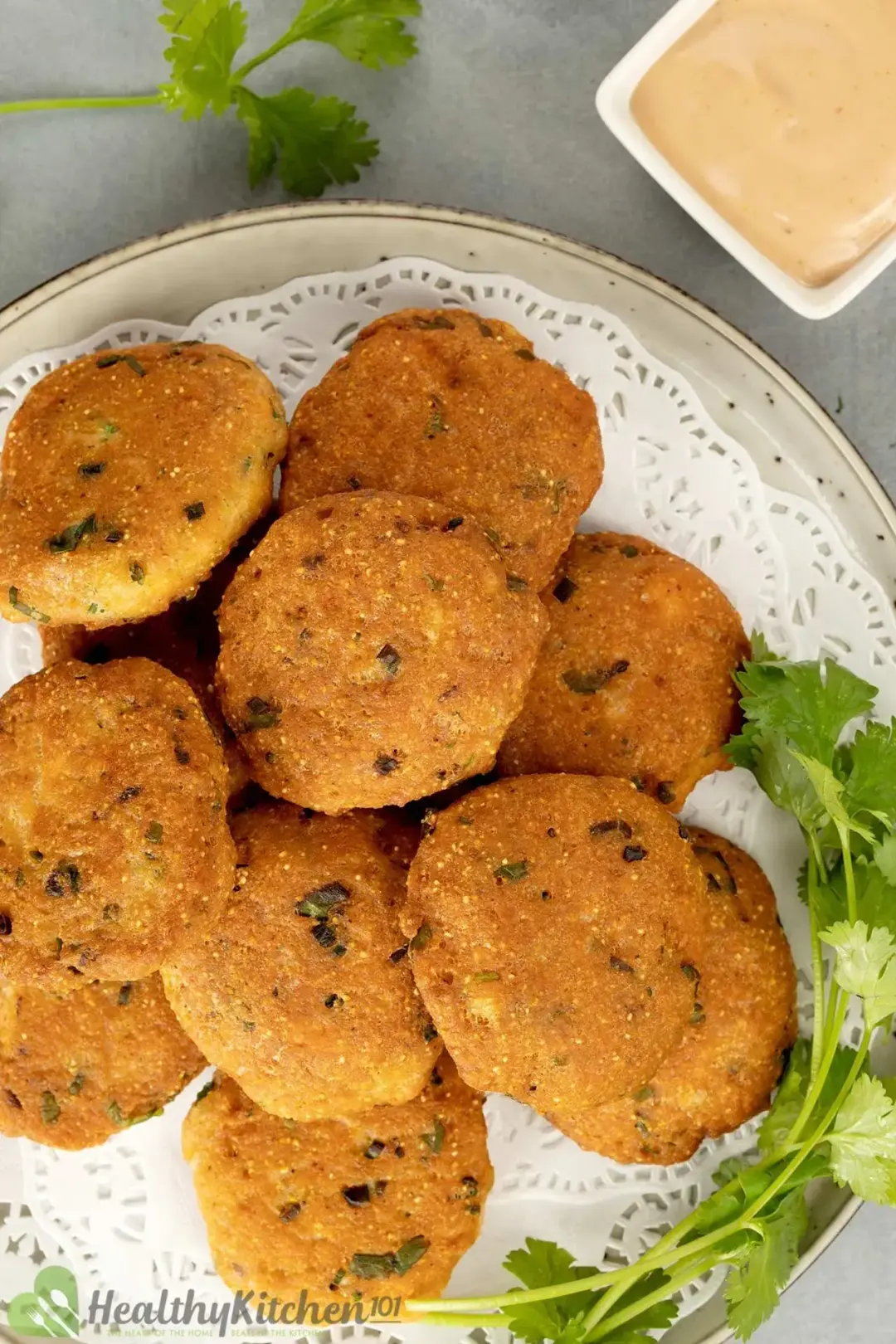 A plate of salmon patties lined with white paper, garnished with cilantro and next to a dipping sauce