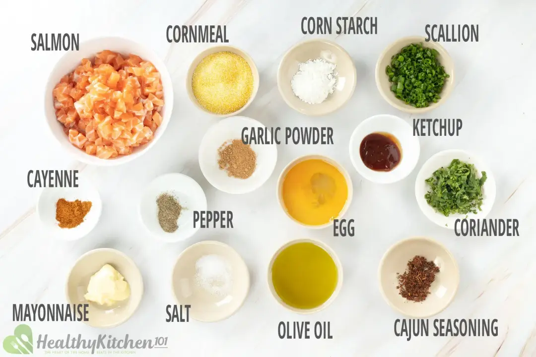 Ingredients in separate bowls: cubed raw salmon, cornmeal, a beaten egg, fresh herbs and spices