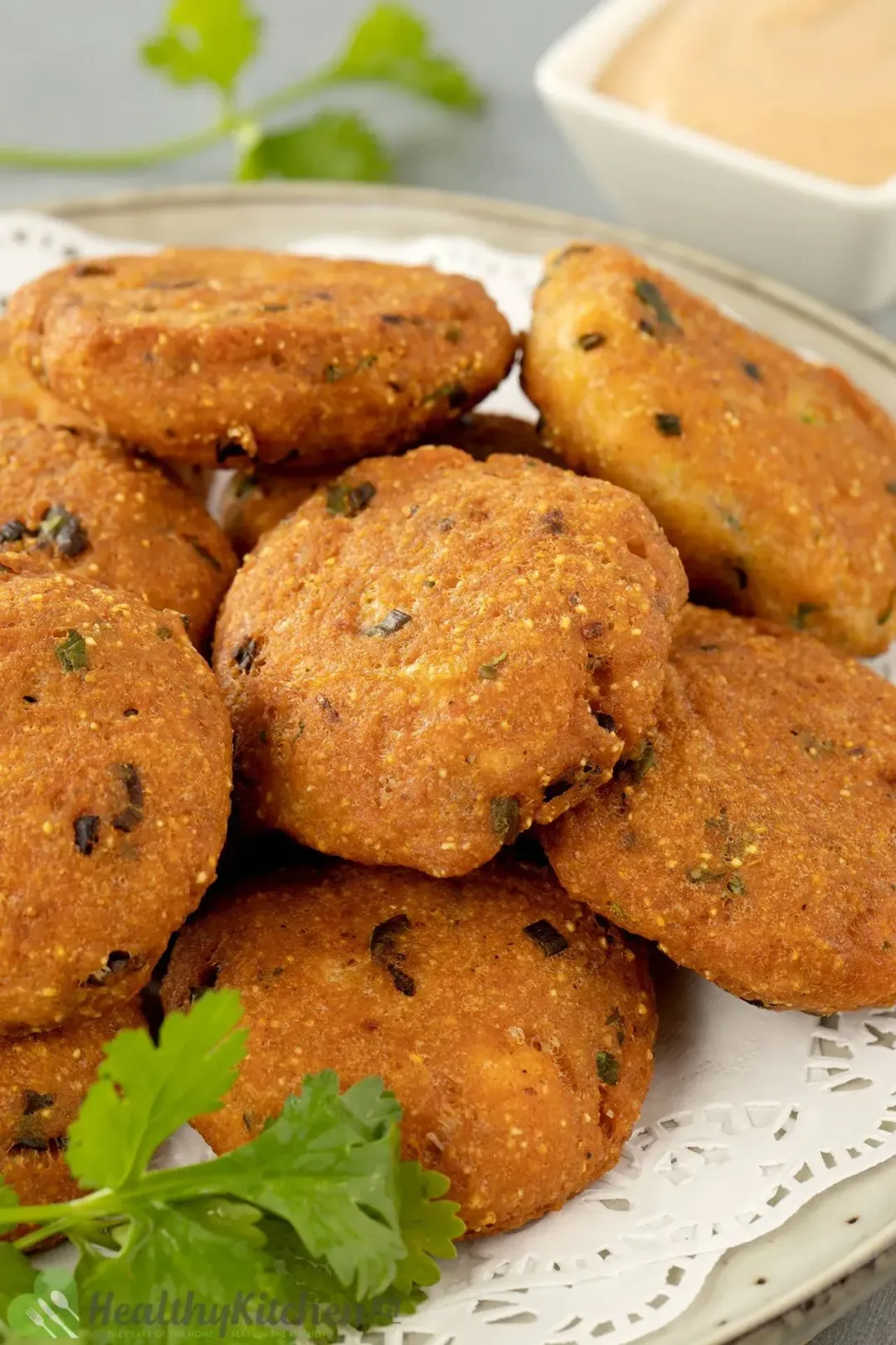 A plate of salmon patties lined with white paper, garnished with cilantro and next to a dipping sauce