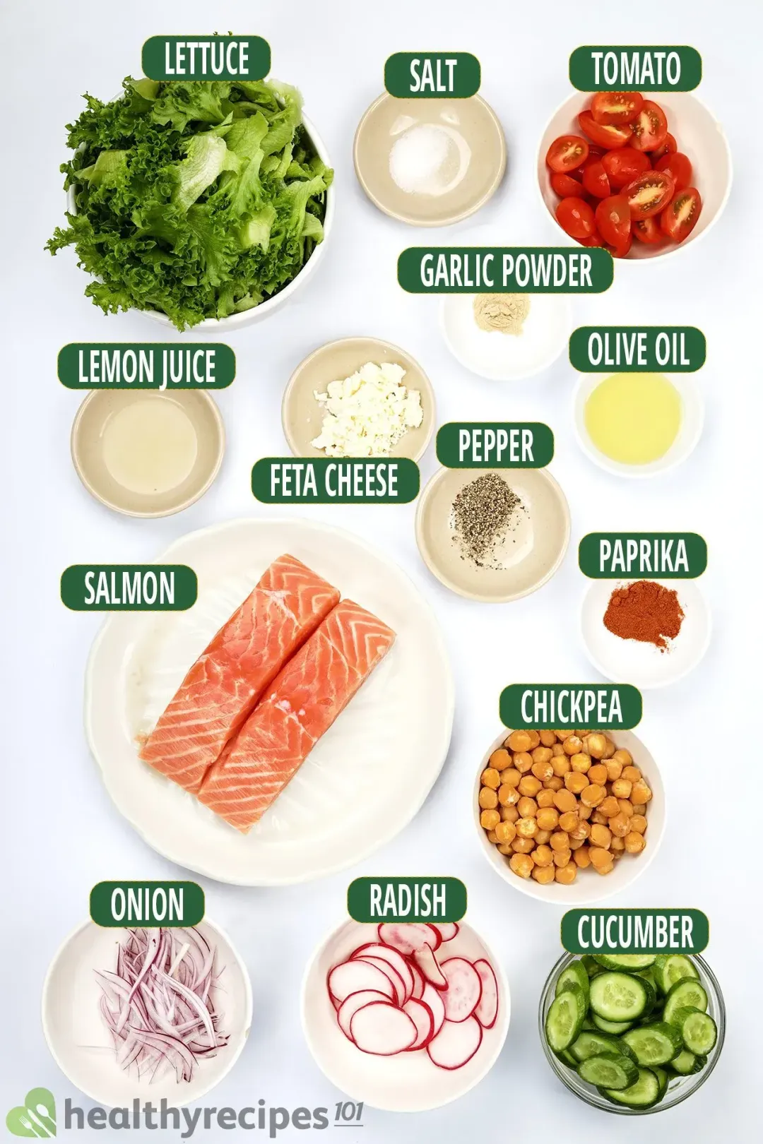 A round white plate containing two raw salmon fillets, a bowl of lettuce, a bowl of halved cherry tomatoes, and a bowl of chickpeas laid near various spices and condiments