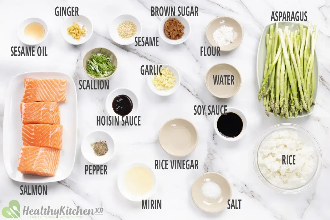 A full display of ingredients in separate bowls: salmon filets, ginger, sesame oil, scallion, hoisin sauce, pepper, brown sugar, sesame, garlic, flour, water, soy sauce, rice vinegar, mirin, salt, asparagus, and rice.
