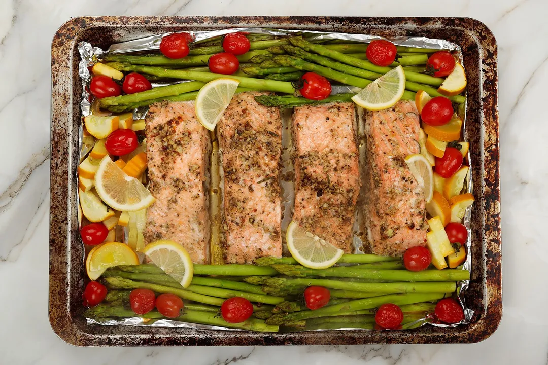 baked salmon on a baking tray with potato cubes, cherry tomato, asparagus