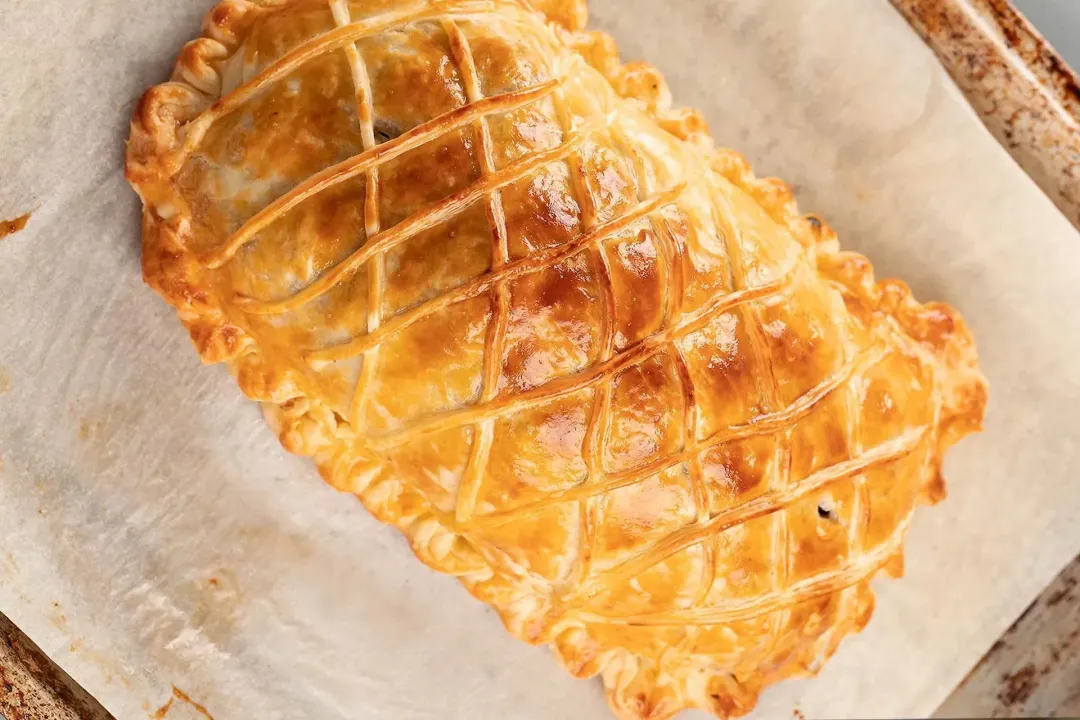 A high angle shot of a golden and freshly-baked salmon en croute laid on a baking pan lined with parchment paper