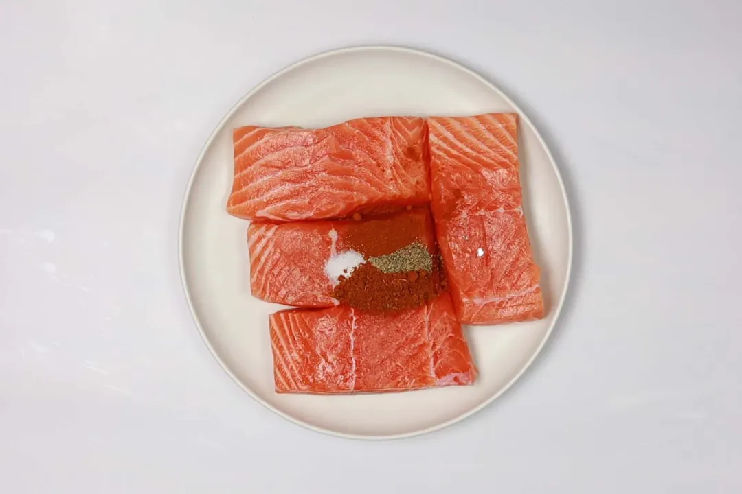 A plate of four salmon fillets with some spices on top.