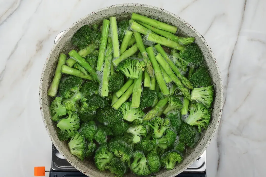 A picture of some asparagus and broccoli florets being boiled in a large pot of water