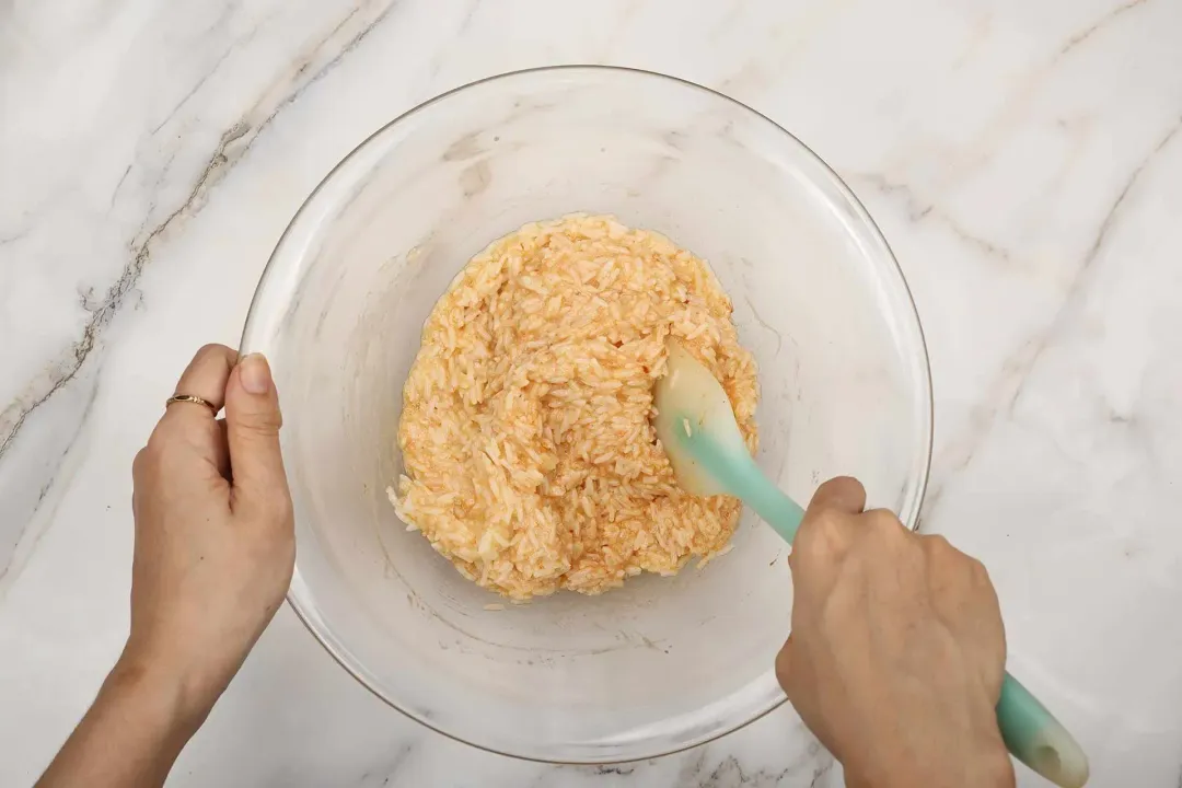 Golden cooked rice mixed with seasonings with a blue spatula in a clear bowl