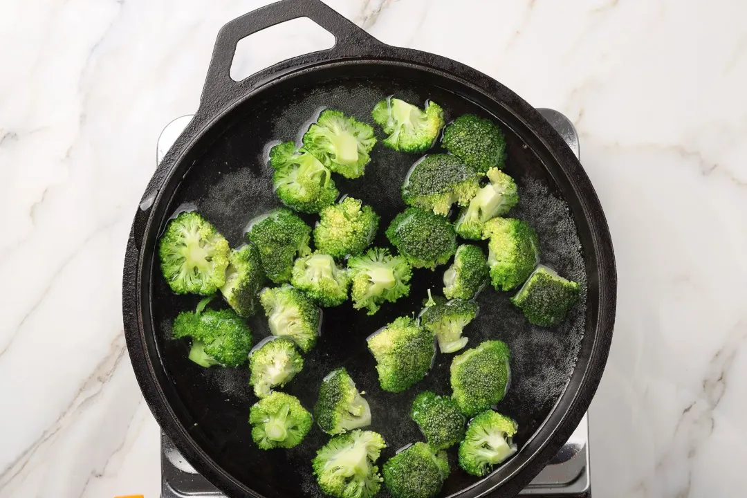A picture of some broccoli florets being boiled in a cast iron pan half-filled with water