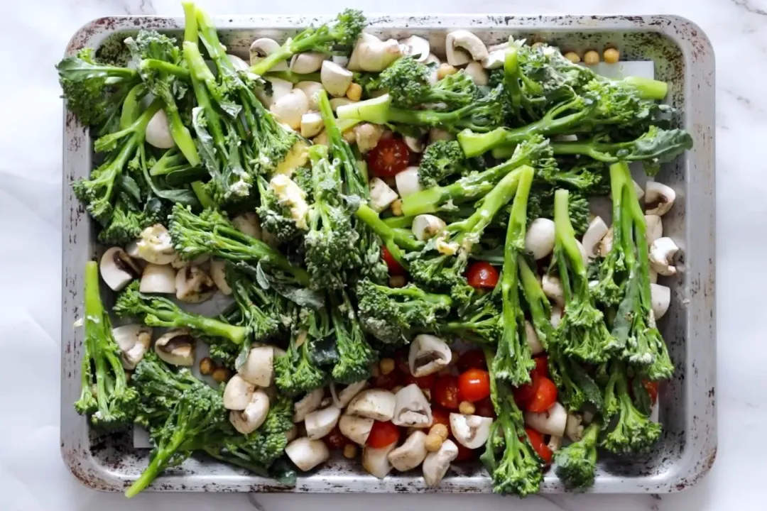 A sheer pan filled with broccolini, sliced white mushrooms, and halved cherry tomatoes