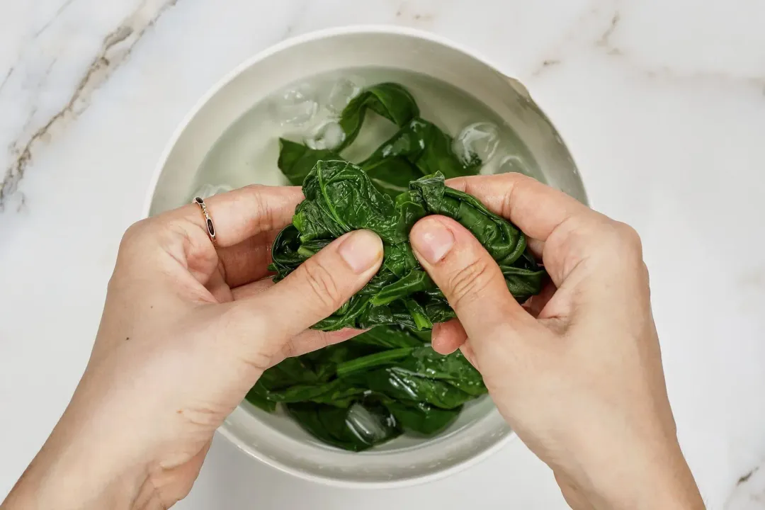 A picture of some blanched spinach and basil being transferred to a bowl of ice water