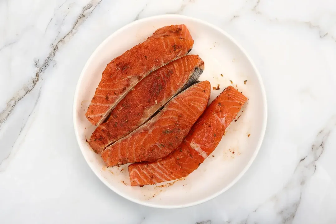 A round white plate containing four raw salmon fillets