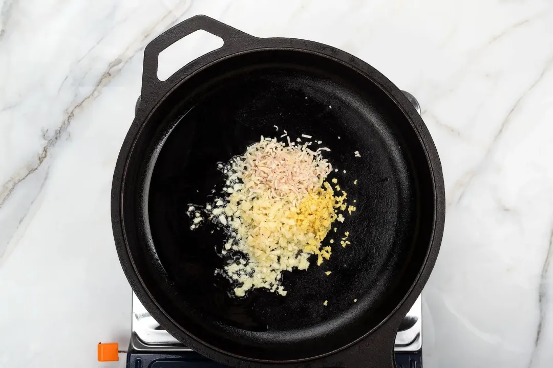 A skillet cooking finely minced garlic, minced ginger, and finely minced lemongrass