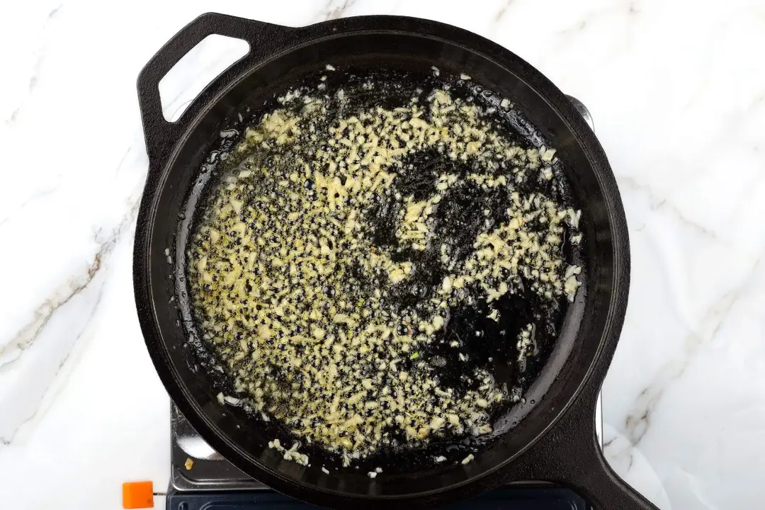 A skillet cooking minced garlic with butter