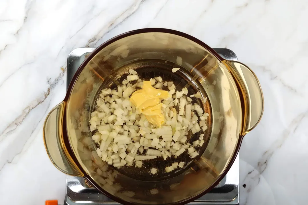 A glass saucepan cooking coarsely-chopped onion with a few dollops of butter