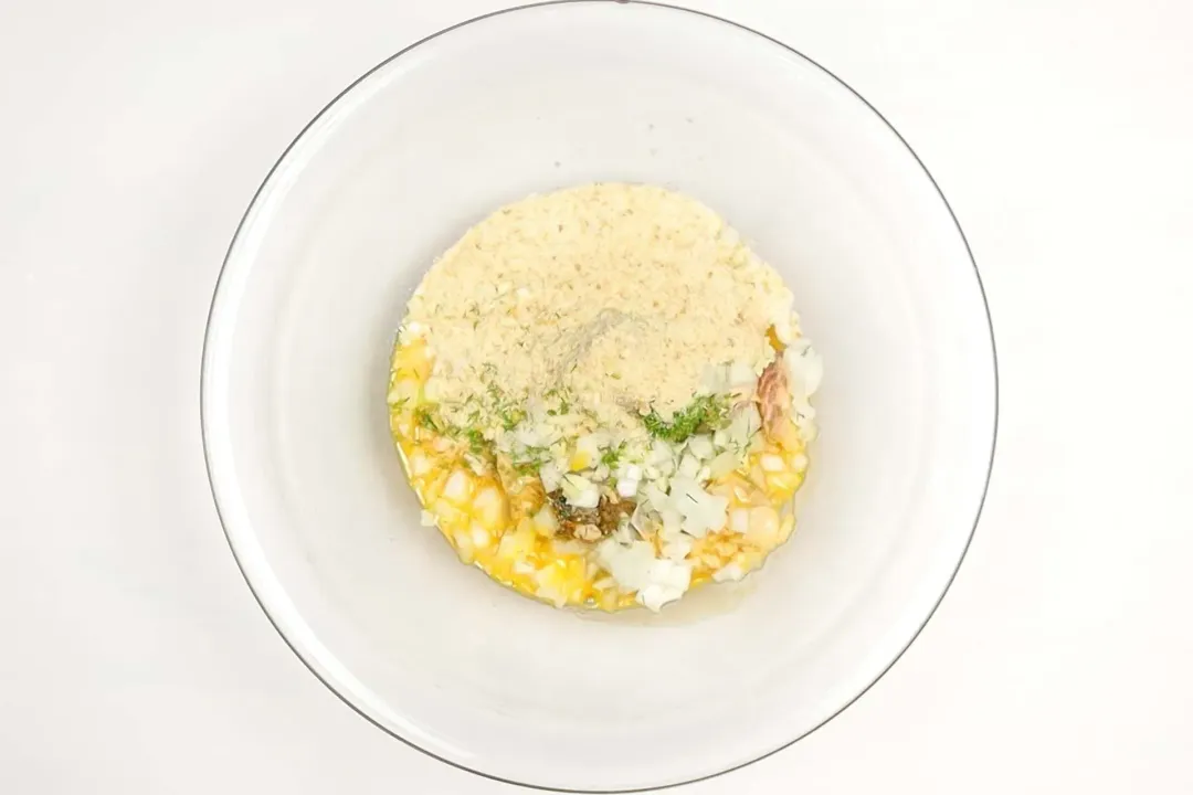 A large glass bowl containing a mixture of canned salmon, veggies, breadcrumbs, and various spices