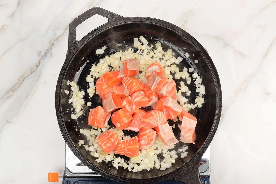 cooking salmon cubes with onion and garlic on a cast iron skillet