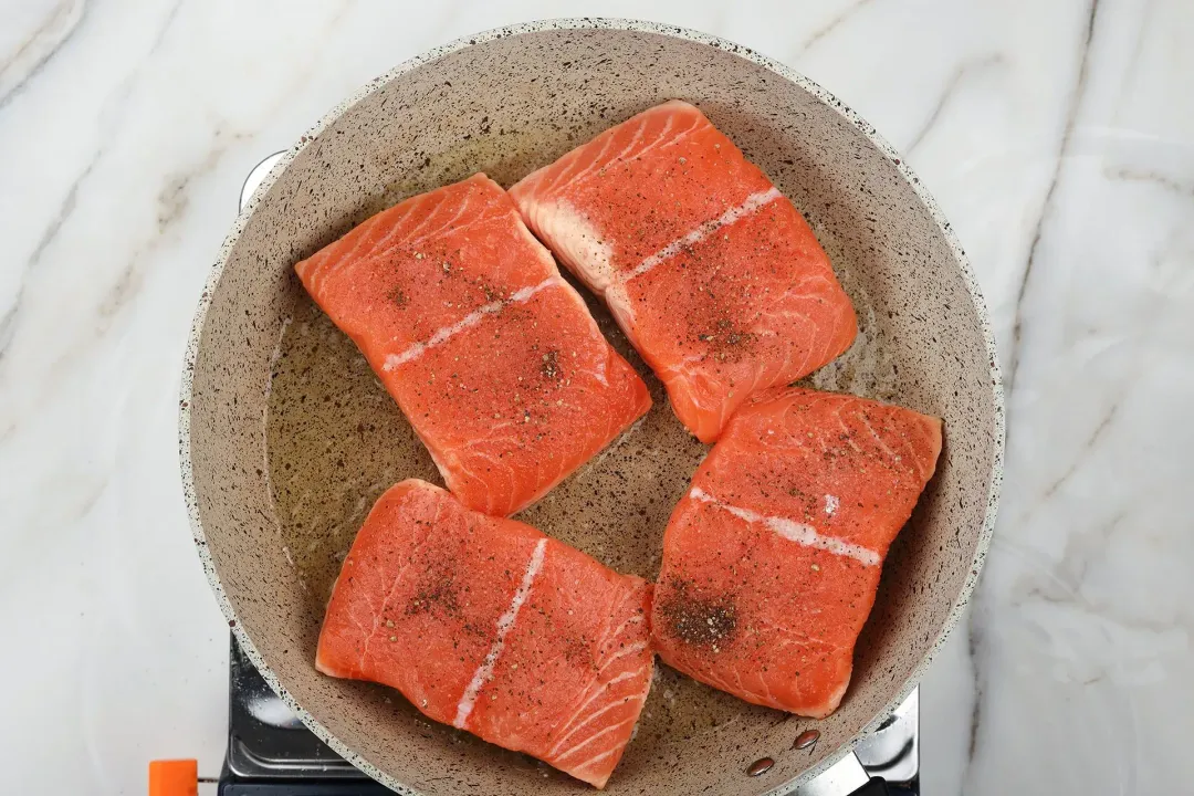 A picture of four salmon fillets being pan-seared on a large non-stick pan