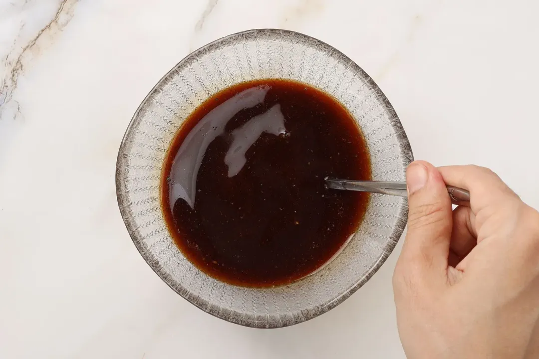 A small bowl of sauce being mixed with a metal spoon