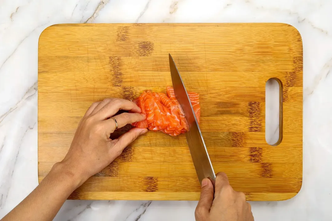 Slicing raw salmon on a wooden cutting board