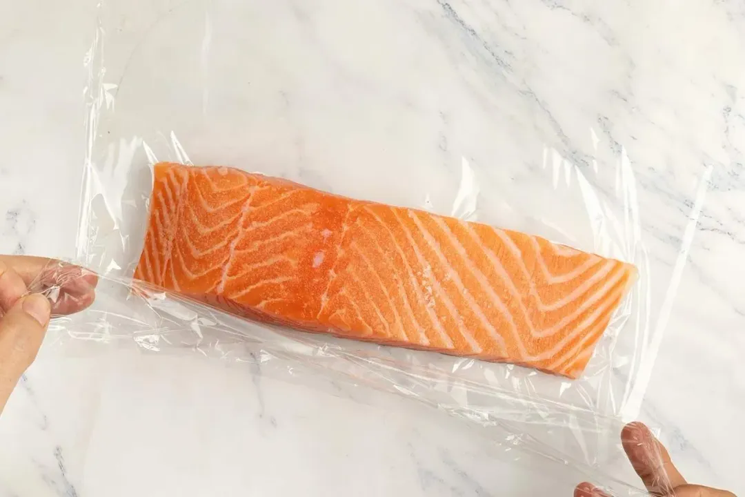 A boneless salmon fillet being wrapped in plastic wrap