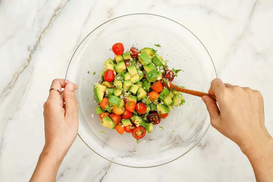 Mixing avocado tomato salsa in a mixing bowl