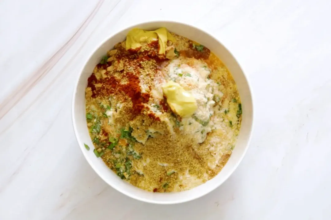 A bowl of mashed salmon mixed with bread crumbs, egg wash, and other spices and herbs.