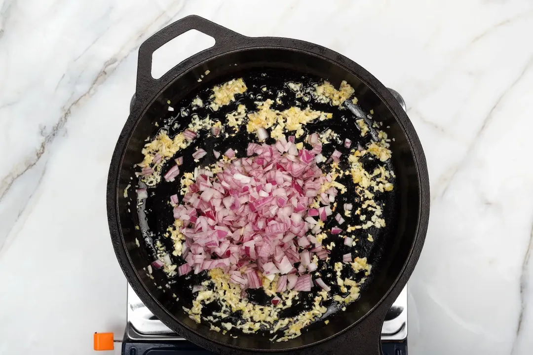 A skillet cooking finely minced aromatics with diced red onion