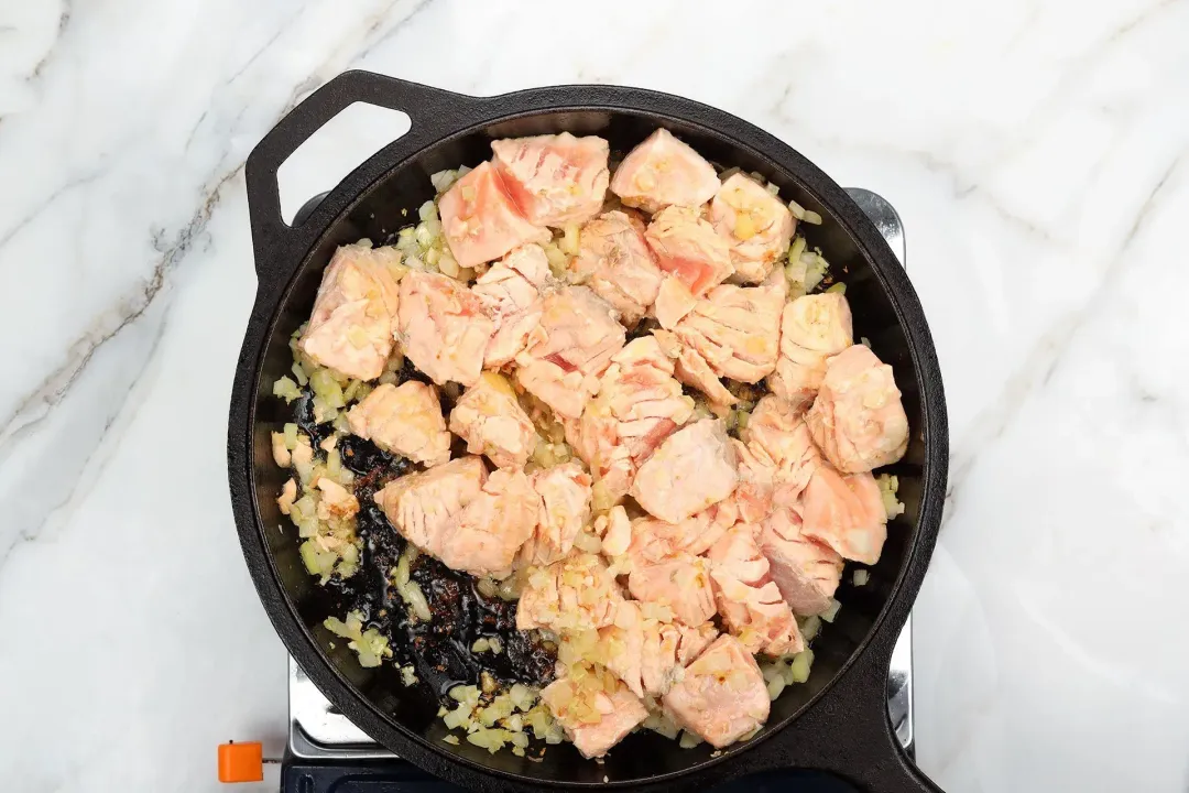 A skillet cooking raw salmon whose flesh is pale pink