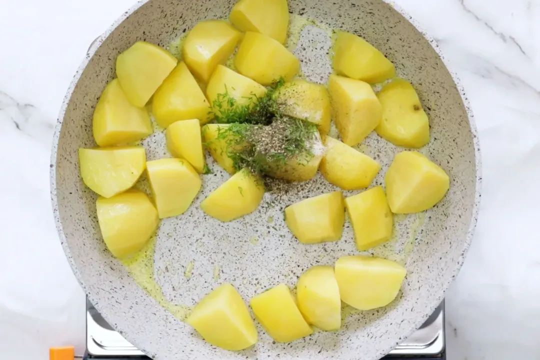 Potato wedges in a gray pan with some chopped dills and seasonings in the middle