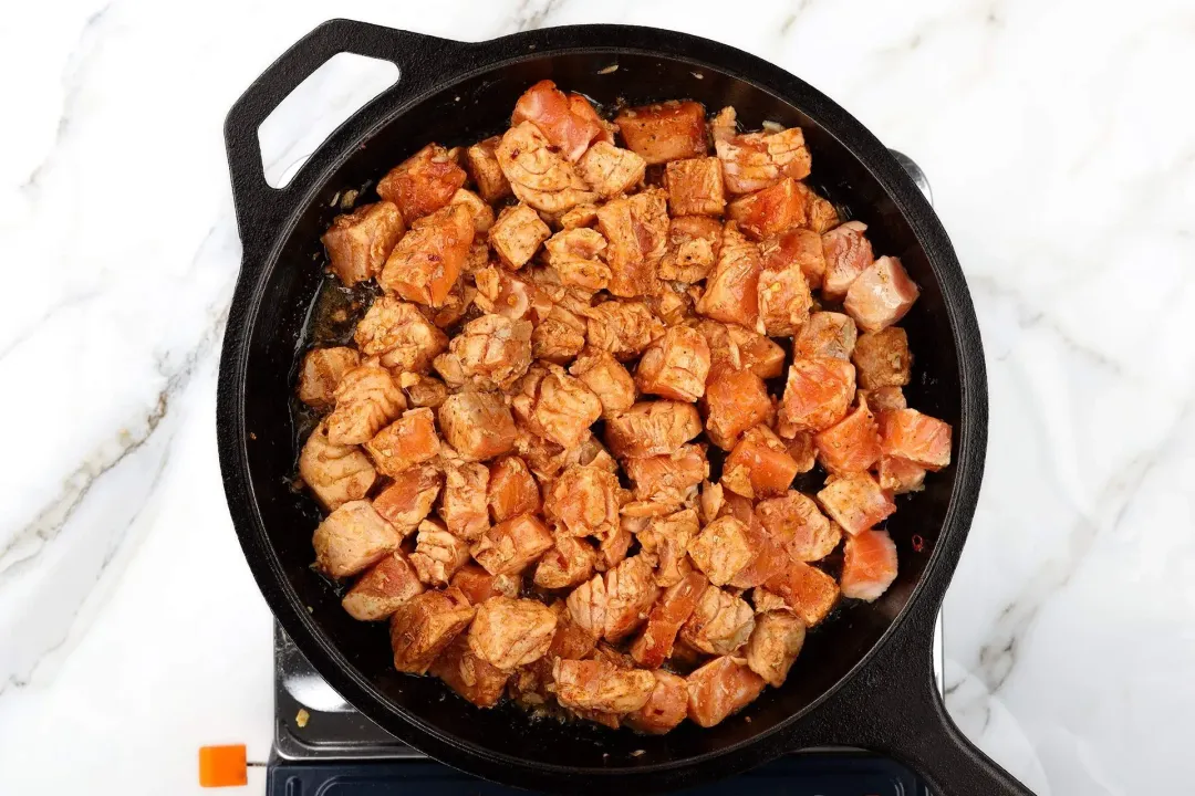 A skillet cooking cubed salmon that are bright orange