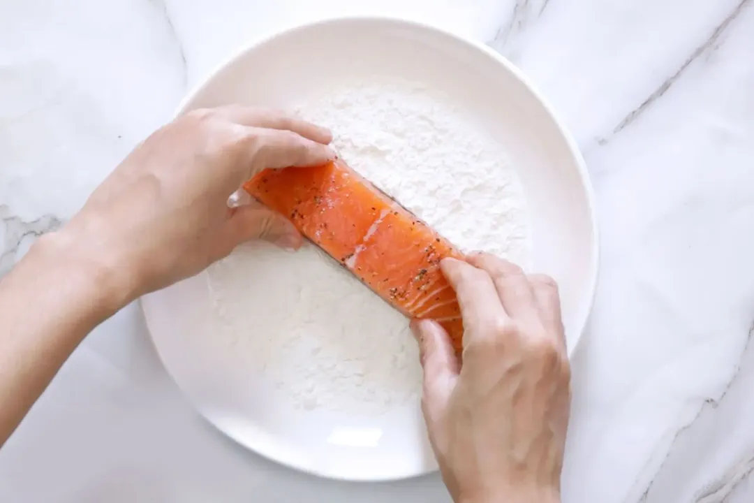 A raw salmon filet is being dredged in flour.