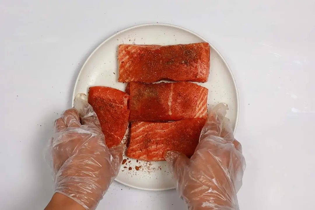  Two hands touching the salmon fillets on a plate with some spices on top.