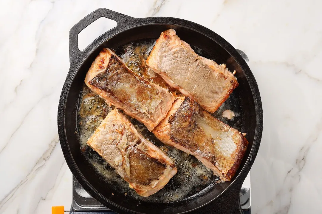 A picture of four salmon fillets being seared with olive oil in a cast iron skillet