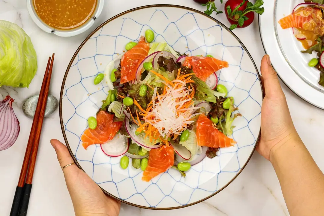 A plate of Japanese Salmon Salad alongside a small bowl of sesame dressing and a pair of chopsticks